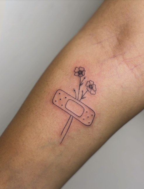 Fine line tattoo of a plaster with two flowers growing through it