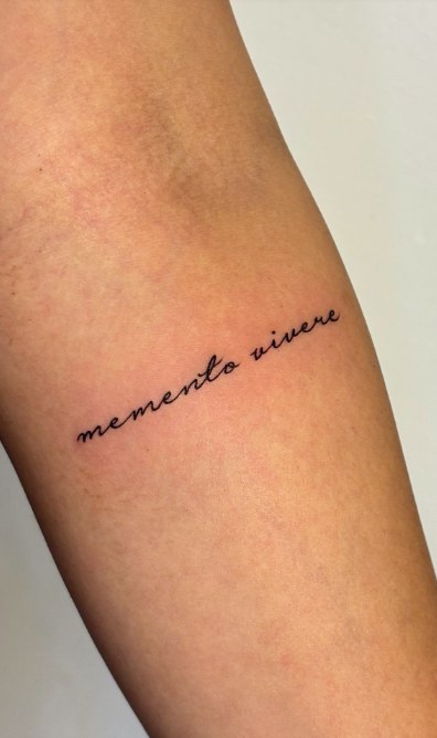 Fine cursive script tattoo reading memento vivere on a forearm