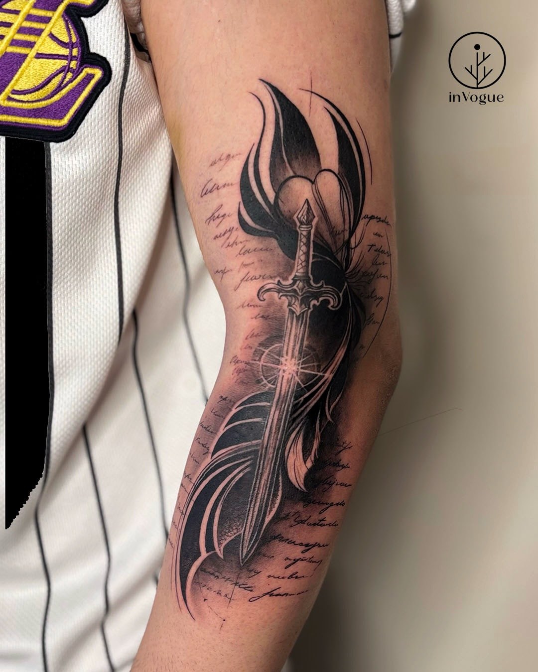 Black and grey sword tattoo wrapped in handwritten script on an upper arm