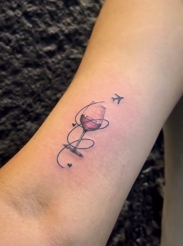 Small fine line tattoo of a wine glass, plane and looping line